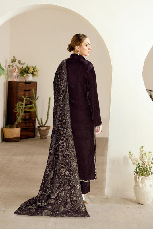Woman wearing a dark outfit with a floral cape in a minimalistic room.