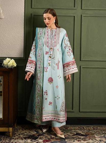 Woman in a light blue embroidered dress standing in a room with green walls and a wooden cabinet.