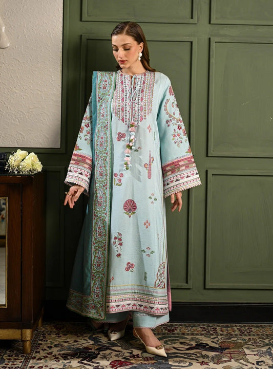 Woman in a light blue embroidered dress standing in a room with green walls and a wooden cabinet.