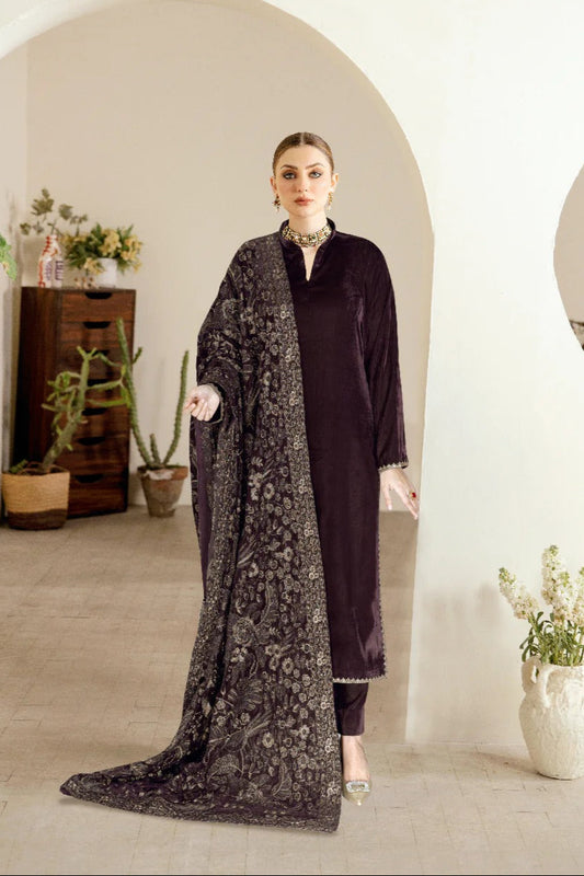 Woman in a plum colored velvet outfit with a long black embroidered shawl in a room with decorative plants.