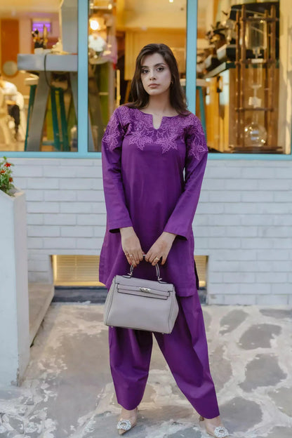 Woman in a purple outfit standing in front of a store window.